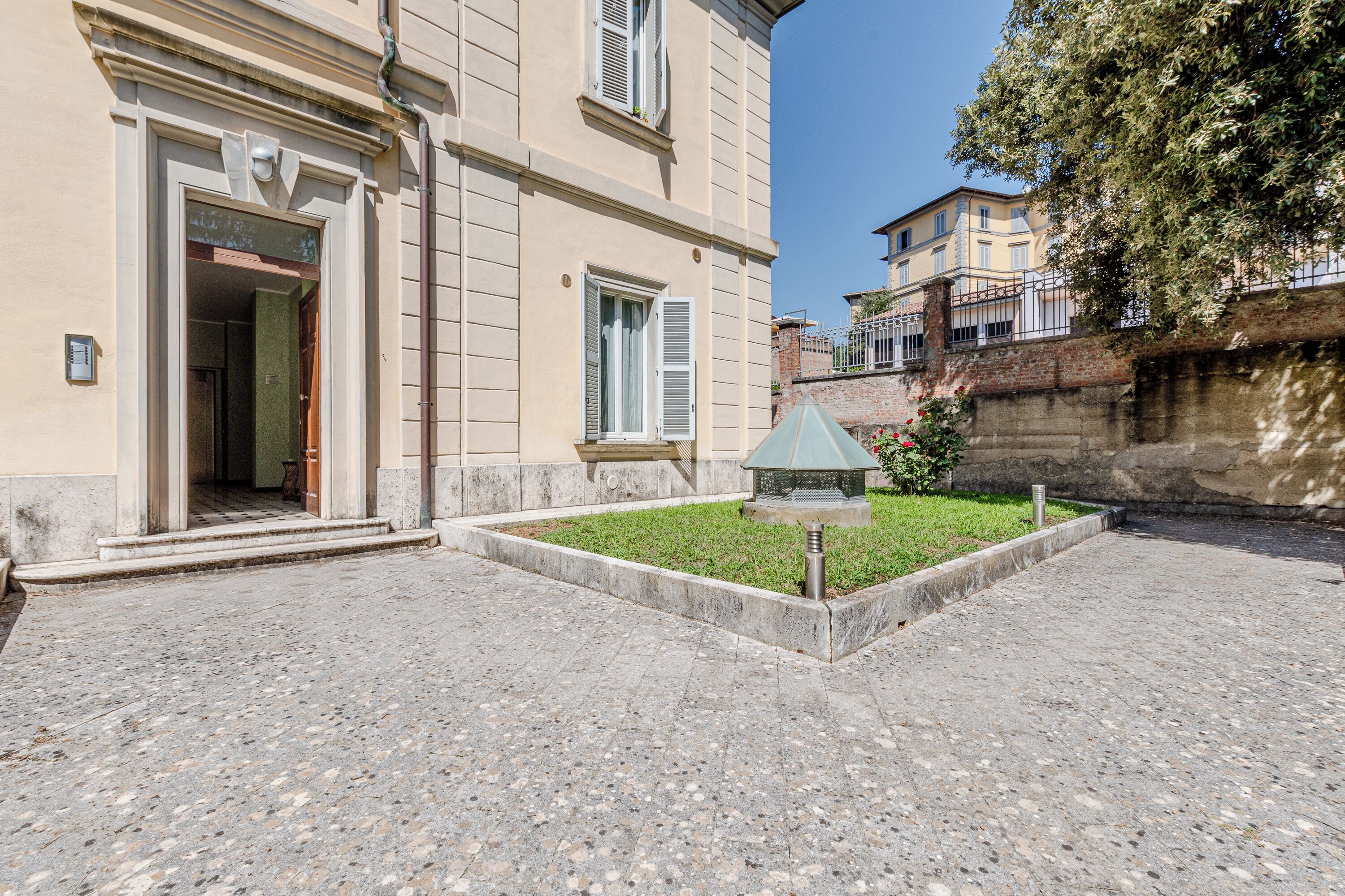 Un bâtiment doté d’une cour dallée, d’un petit jardin agrémenté d’un lampadaire en métal et d’une porte donnant sur un espace intérieur.