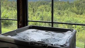 Een bubbelbad met uitzicht op een bebost berglandschap door grote ramen.