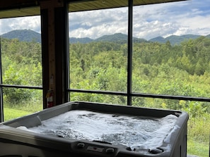 Ein Whirlpool mit Blick auf ein bewaldetes Gebirge durch große Fenster.