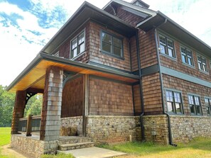Ein zweistöckiges Haus mit Stein Fundament und Holzverkleidung, mit einer überdachten Veranda und Steinreling.