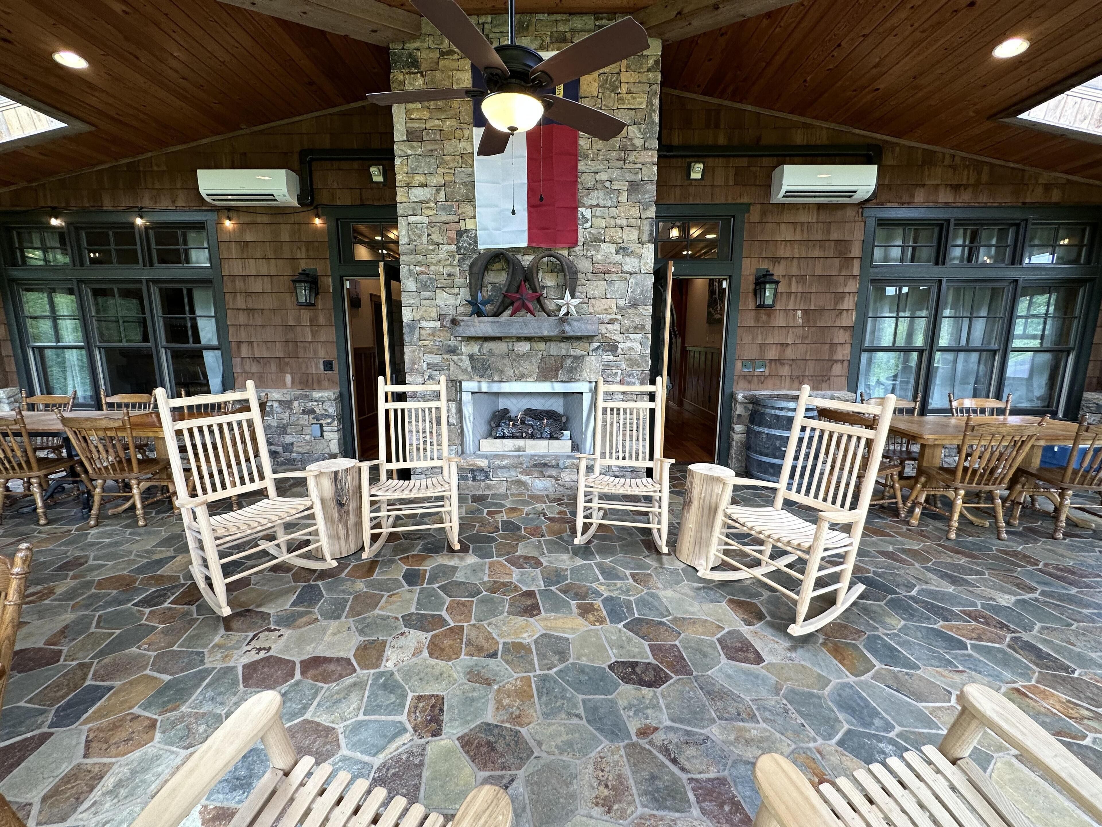 Eine Terrasse mit Steinboden, Holzmöbeln, Kamin und Deckenventilator.