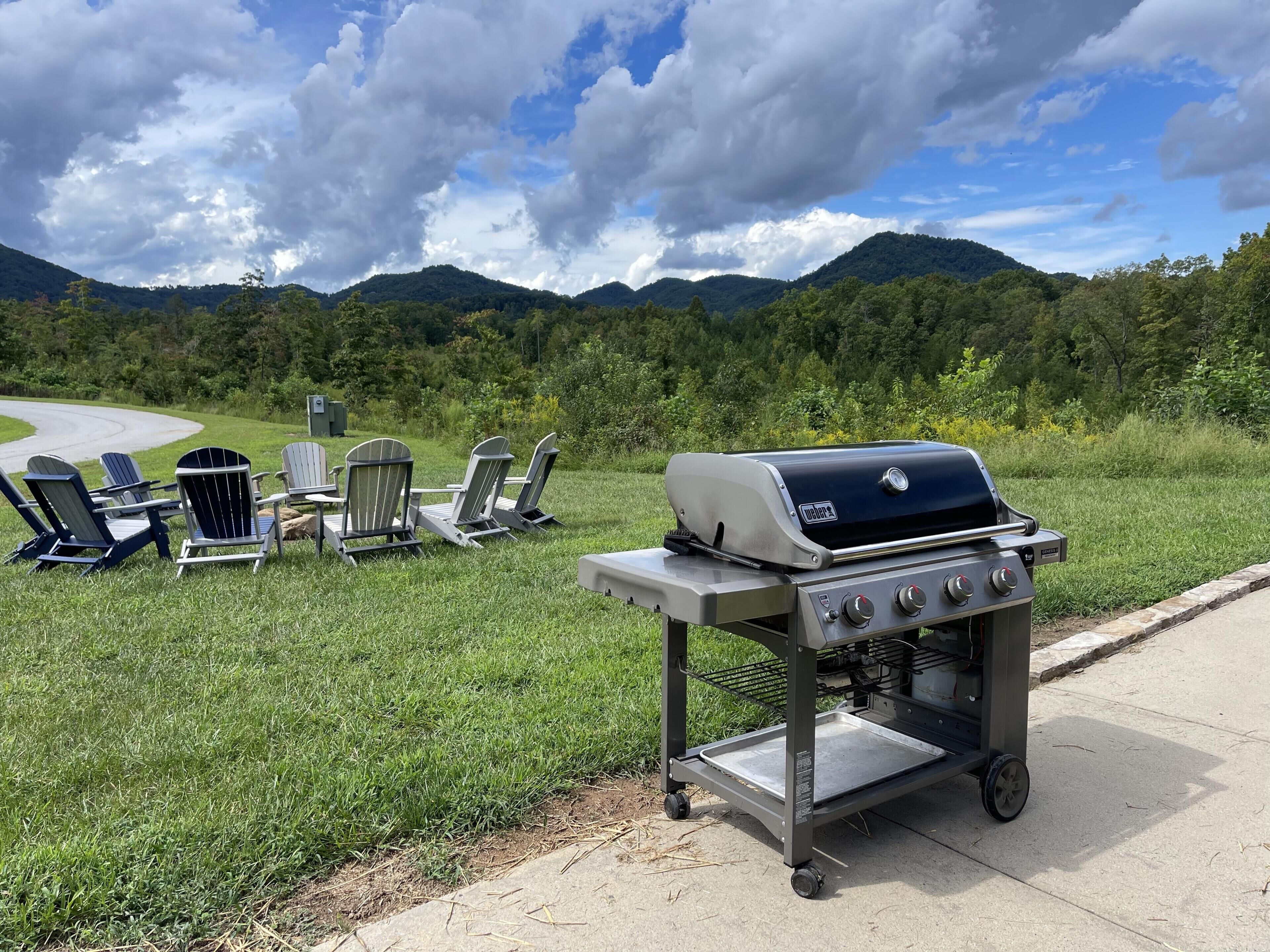Ein tragbarer Grill mit einem Metallgestell, vier Adirondack-Stühlen und einem schönen Blick auf Berge und Bäume.
