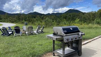 Ein tragbarer Grill mit einem Metallgestell, vier Adirondack-Stühlen und einem schönen Blick auf Berge und Bäume.