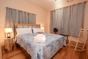 Ein Schlafzimmer mit einem hölzernen Bett, zwei Nachttischlampen, einem Nachttisch aus Holz, einem Schaukelstuhl und einem Fenster mit Vorhängen.