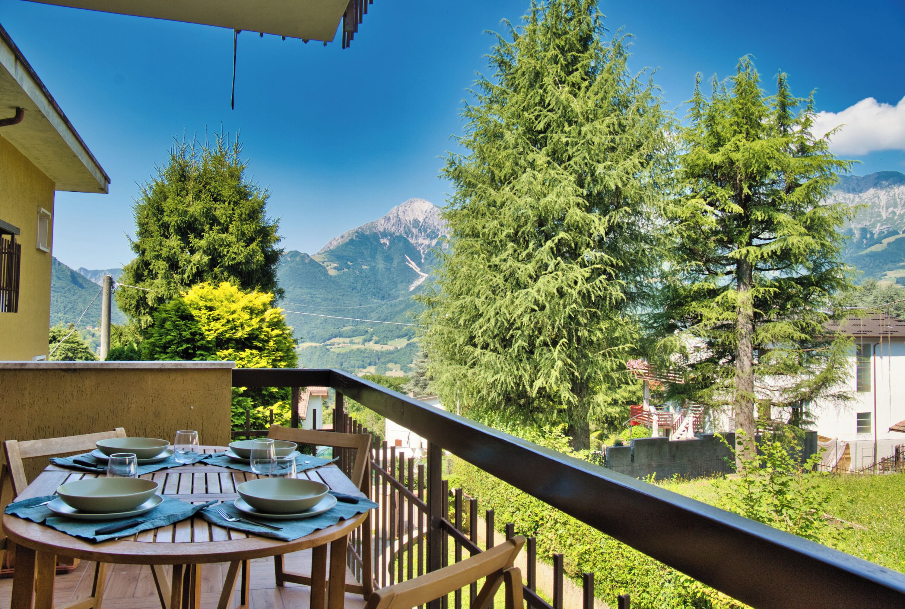 A dining table with plates and glasses, overlooking a mountainous landscape with trees and a clear sky.