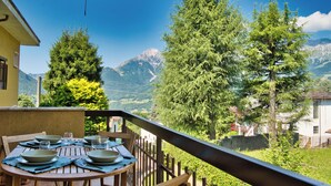 Ein Esstisch mit Tellern und Gläsern, mit Blick auf eine gebirgige Landschaft mit Bäumen und blauem Himmel.