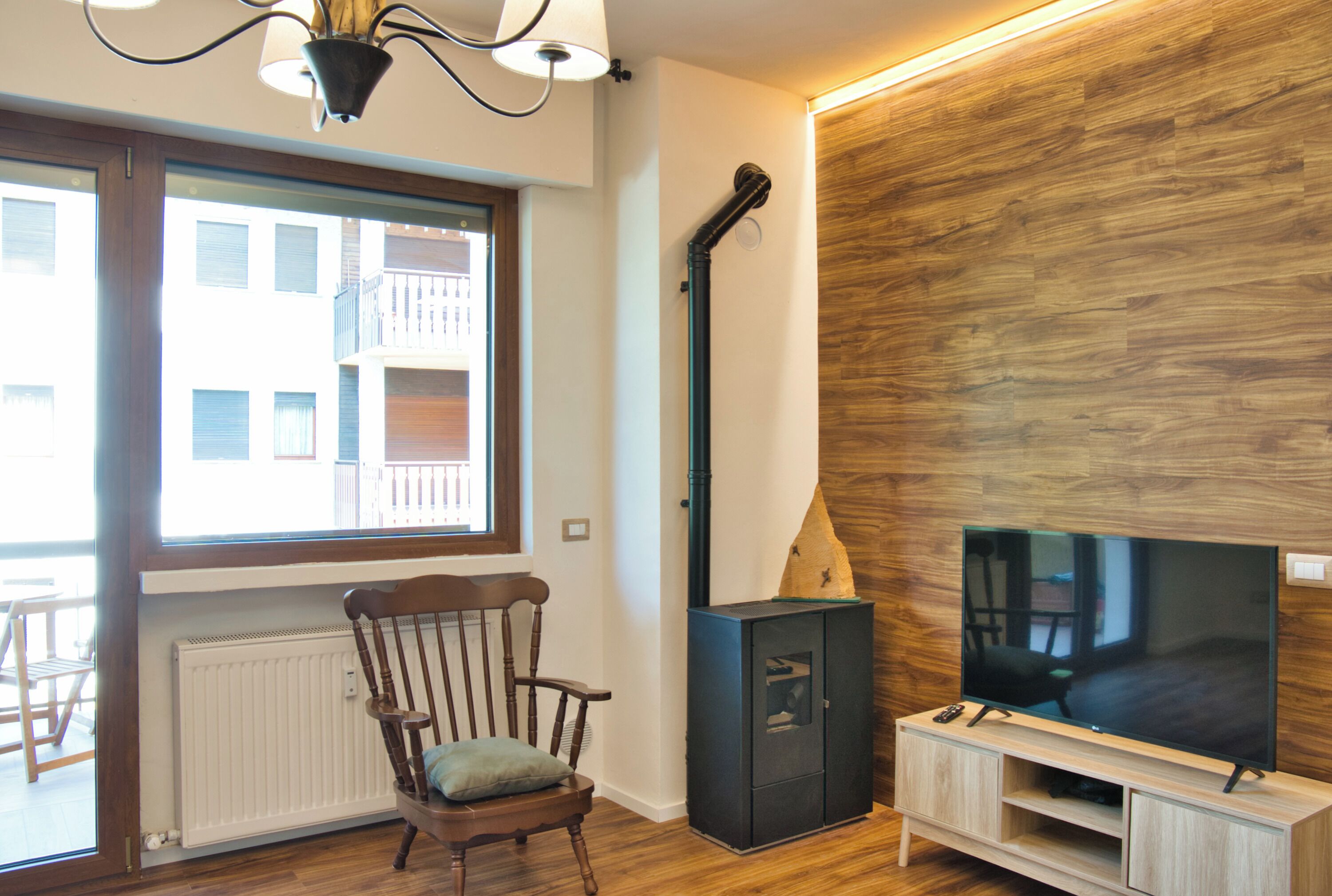 Een moderne woonkamer met een houten vloer, een grote flatscreen televisie, een ingebouwde houten kast, een open haard en een raam met uitzicht op gebouwen.