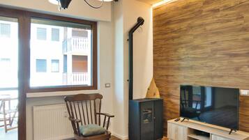 Een moderne woonkamer met een houten vloer, een grote flatscreen televisie, een ingebouwde houten kast, een open haard en een raam met uitzicht op gebouwen.