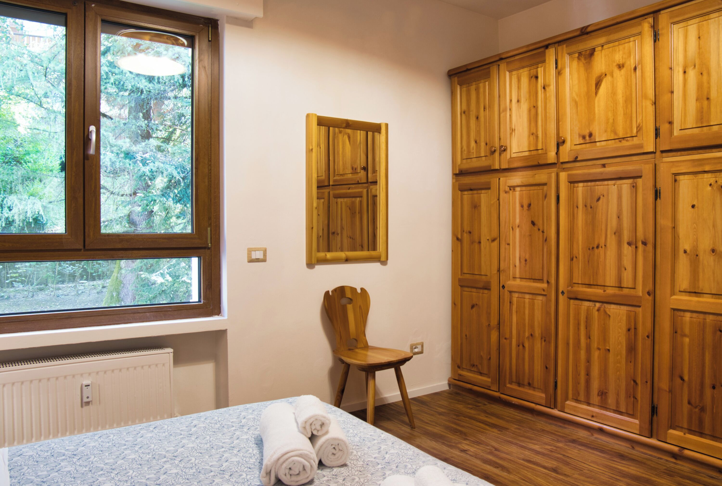 Une pièce avec une grande fenêtre, une armoire en bois et une chaise.