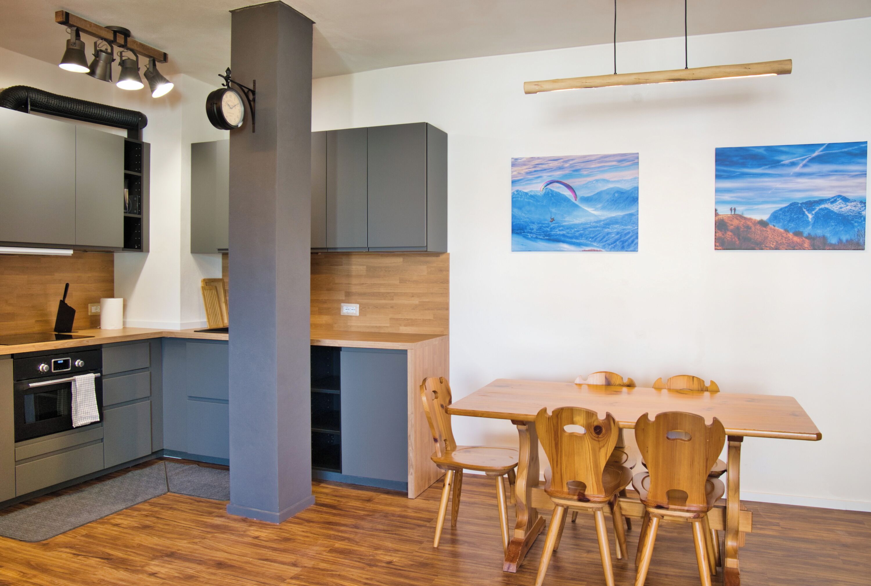 A modern kitchen with grey cabinets, a wooden dining table, and two wooden chairs.
