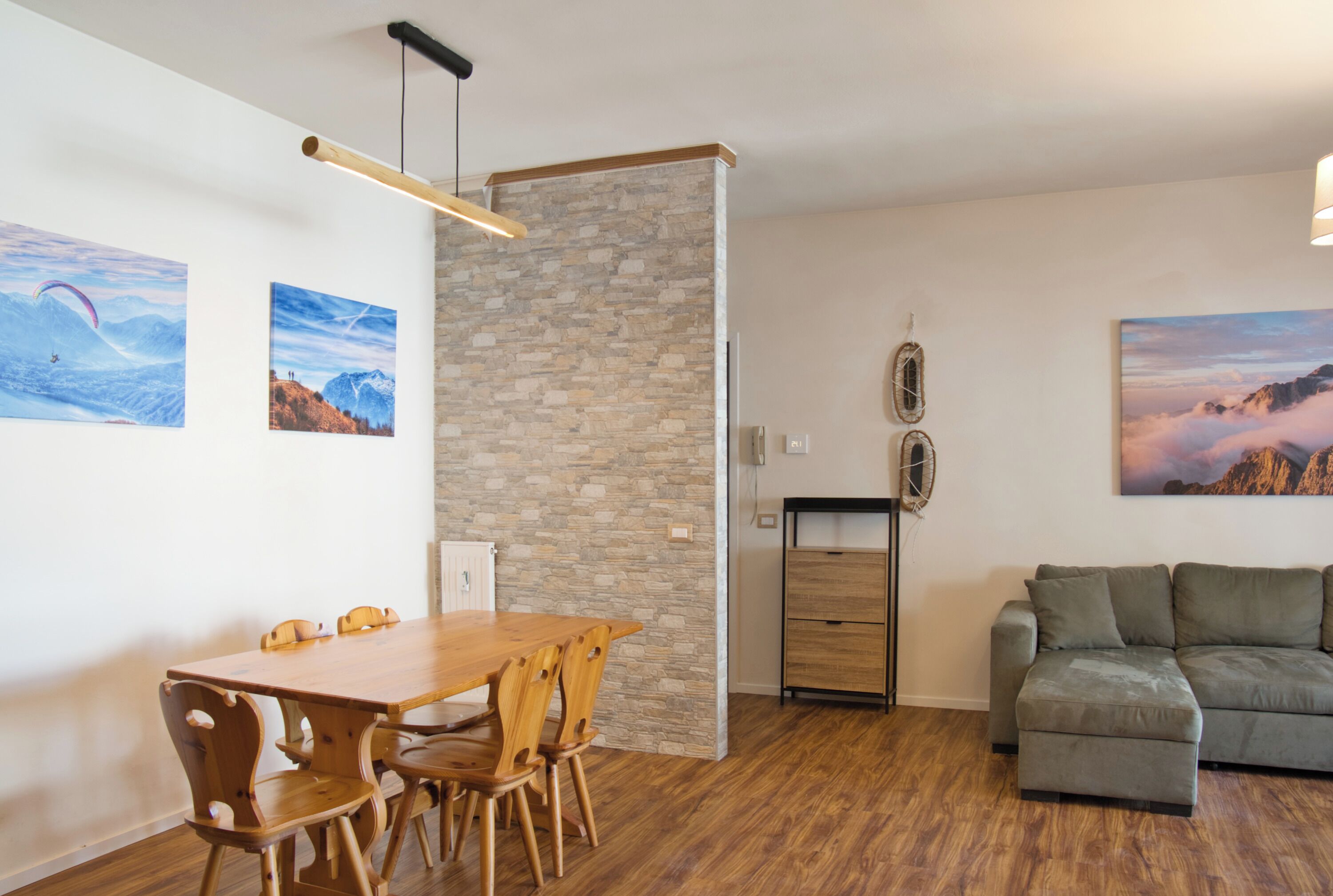 A modern living space with a wooden dining table, a grey sofa, and stone wall accents.