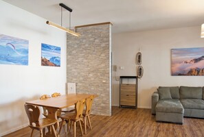 A modern living space with a wooden dining table, a grey sofa, and stone wall accents. - Mountain Escape – Mountain View & Private Sauna (Cassina Valsassina)