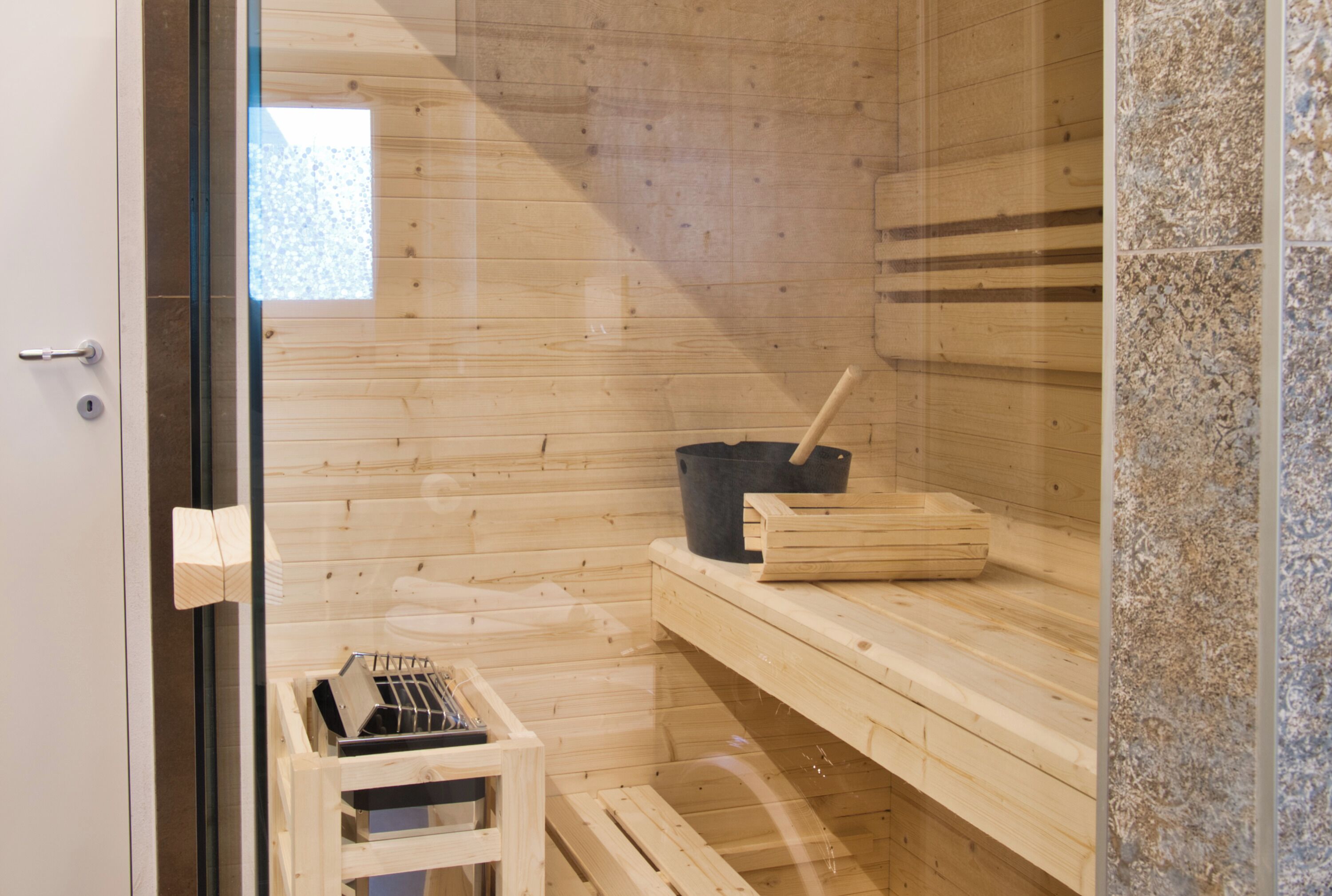 Een sauna met houten wanden, een bankje, een emmer en een houten kist.