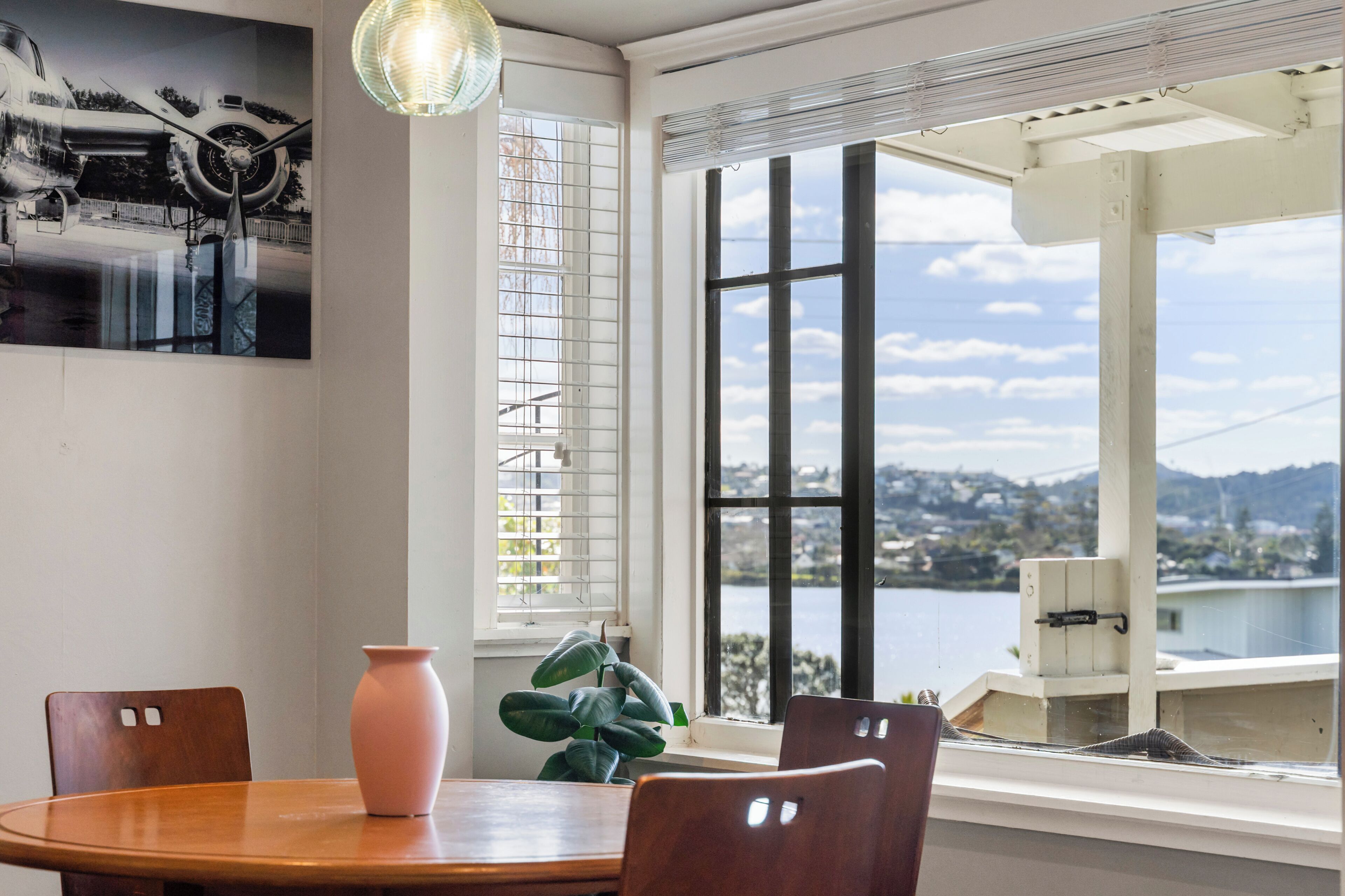 A dining area with a table, chairs, a vase, and a view of a body of water and landscape.