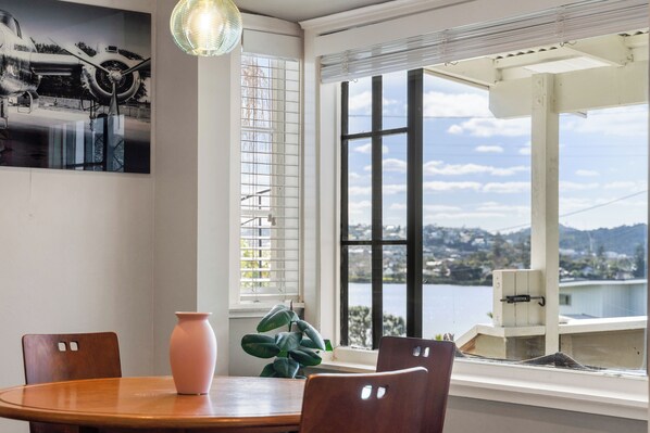 Un espace repas comprenant une table, des chaises, un vase et offrant une vue sur un plan d’eau et un paysage.
