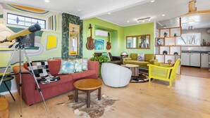 Un salon avec un canapé rouge, un fauteuil blanc et une chaise jaune. On y trouve un télescope sur un trépied, une guitare et un globe terrestre posés sur une table.