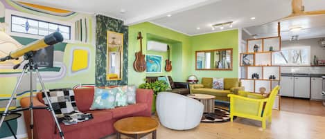 A living room with a red sofa, a white armchair, and a yellow chair. There is a telescope on a tripod, a guitar, and a globe on a table.