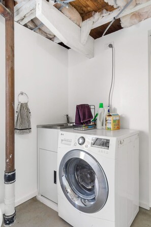 A laundry area with a washing machine, a drying rack, and cleaning supplies. - Rockstar Retreat - Auckland Holiday Home (Red Beach)