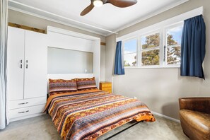Une chambre à coucher avec un lit, une armoire, une fenêtre avec des rideaux et un ventilateur de plafond.
