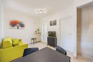 A modern living room with a sofa, a dining table, a TV, and artwork on the wall. - Cozy Nest [Vicino Ospedale Carle] (Cuneo)