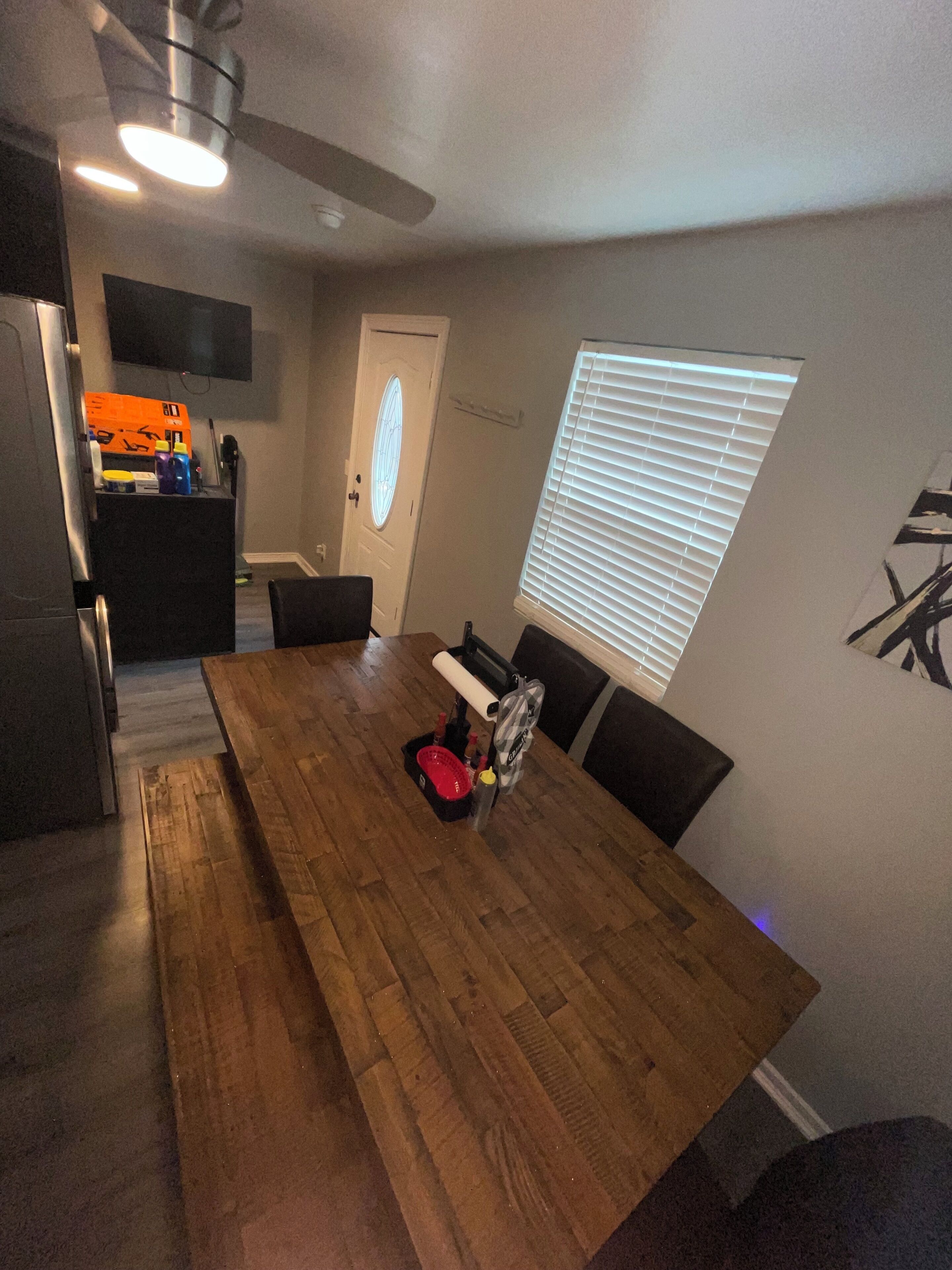 Un coin repas comprenant une table en bois, des chaises, un ventilateur de plafond et une fenêtre avec des stores.