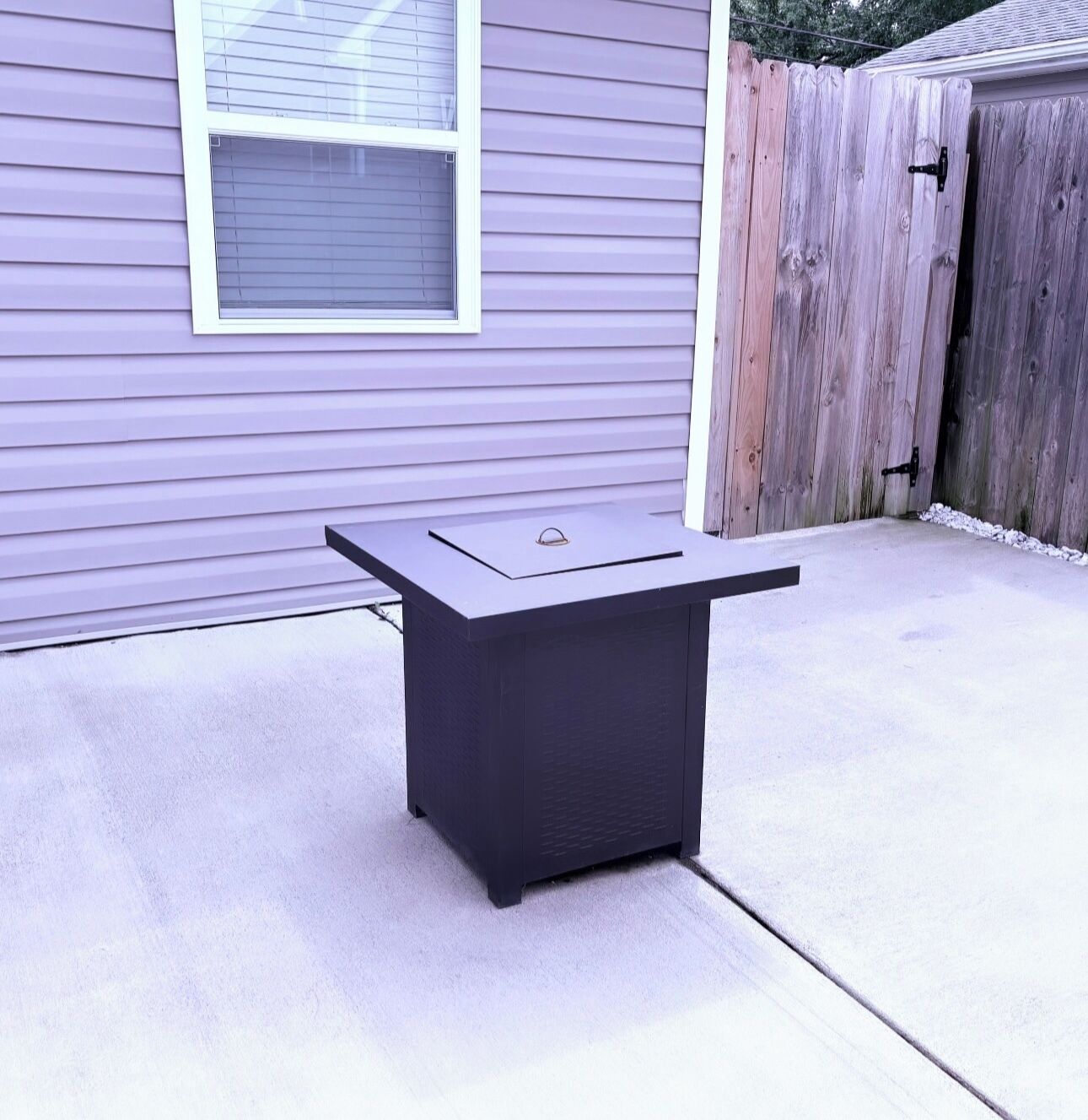 A patio table with a metal top and a dark base, positioned on a concrete surface.