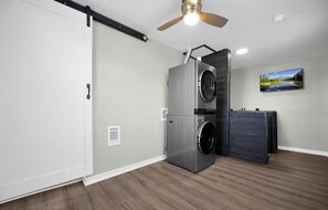 A laundry room with a ceiling fan, a wall-mounted TV, and a large window.
