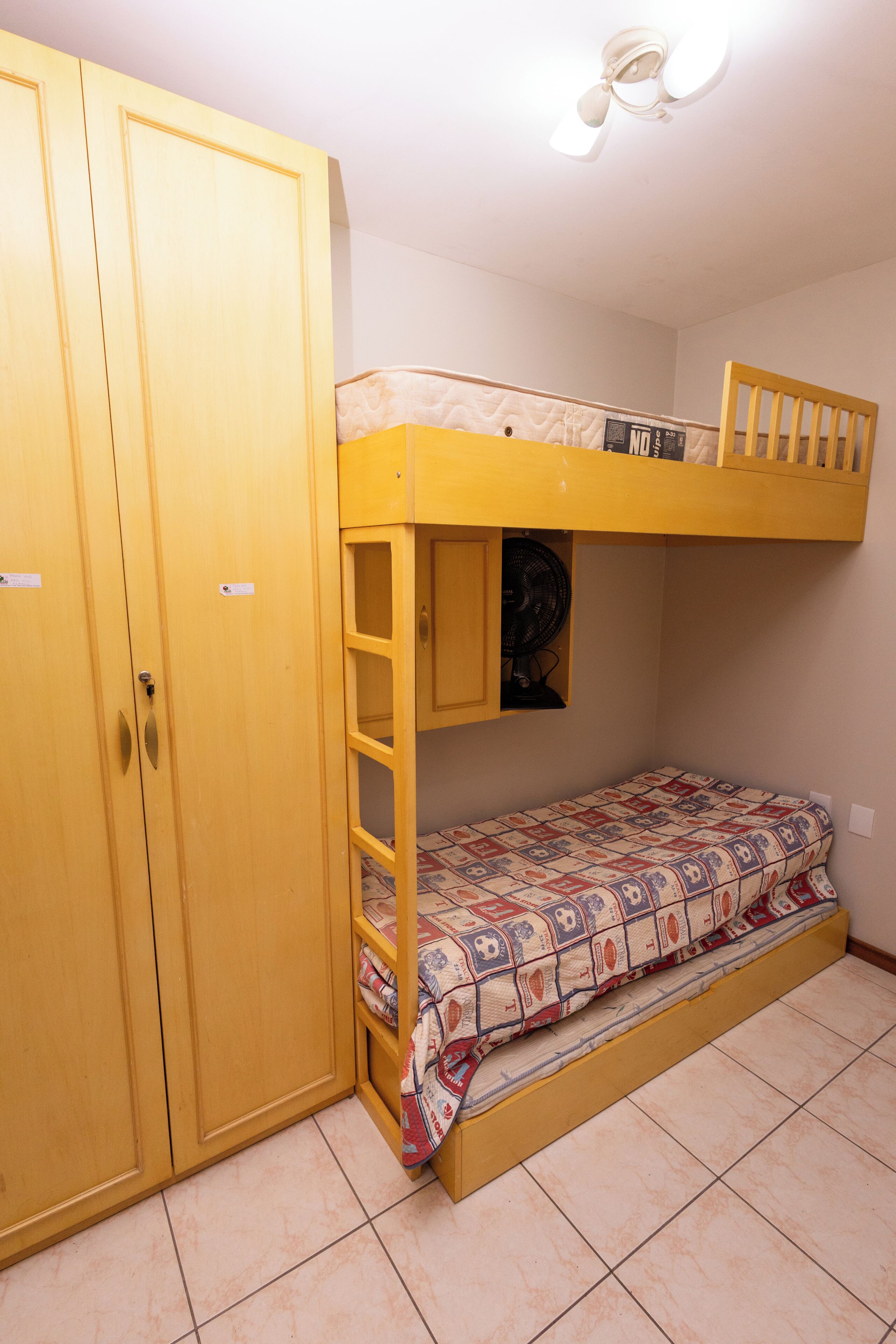 Een stapelbed met een onderbed en een enkel bed, een kledingkast en een plafondventilator.