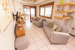 A living room with a sofa, a TV, a wooden side table, and a window.