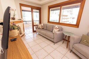 Una sala de estar con un sofá, una mesita, un televisor y una ventana con vistas a edificios.