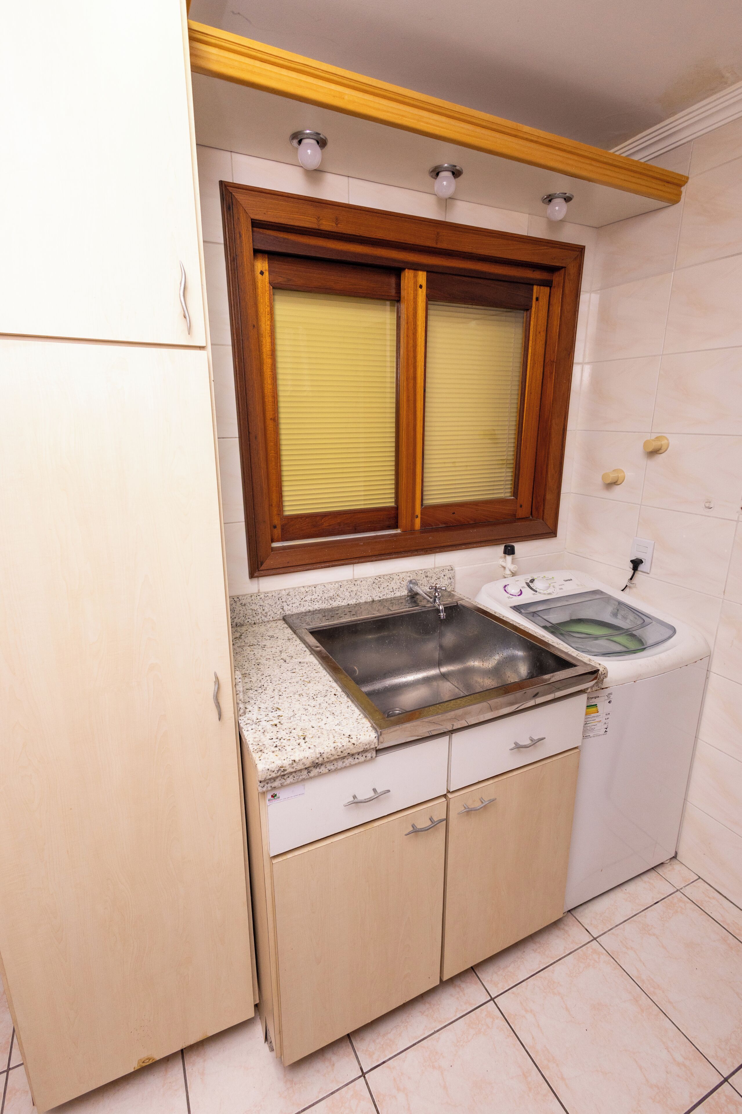 Uma cozinha compacta com pia embutida, moldura de janela de madeira e painel de azulejos.