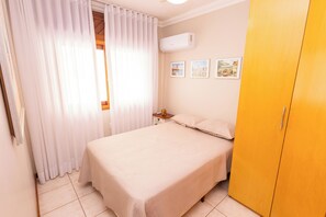 Un dormitorio con cama, mesita de noche, armario y ventana con cortinas.