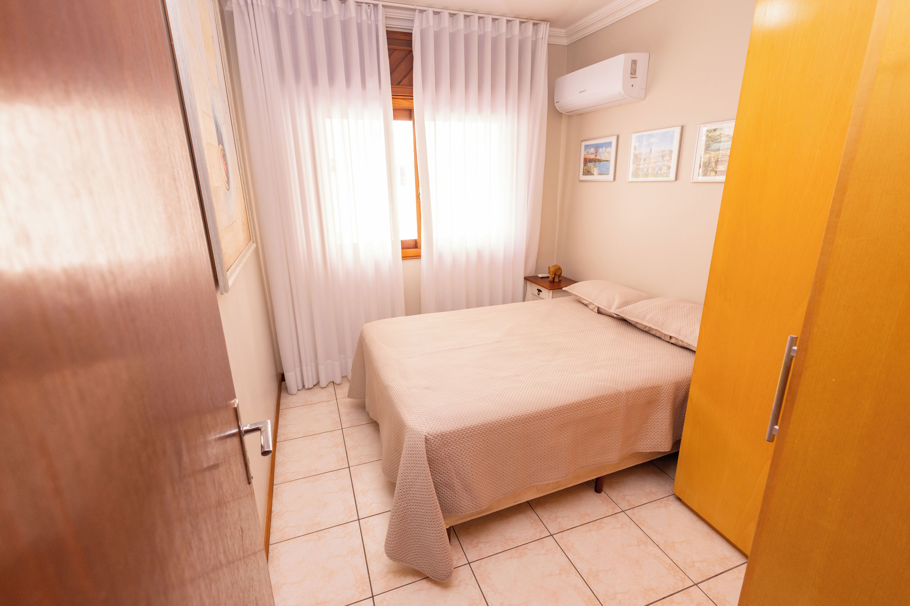 Een slaapkamer met een bed, nachtkastje, raam met gordijnen en een airconditioning op de muur.
