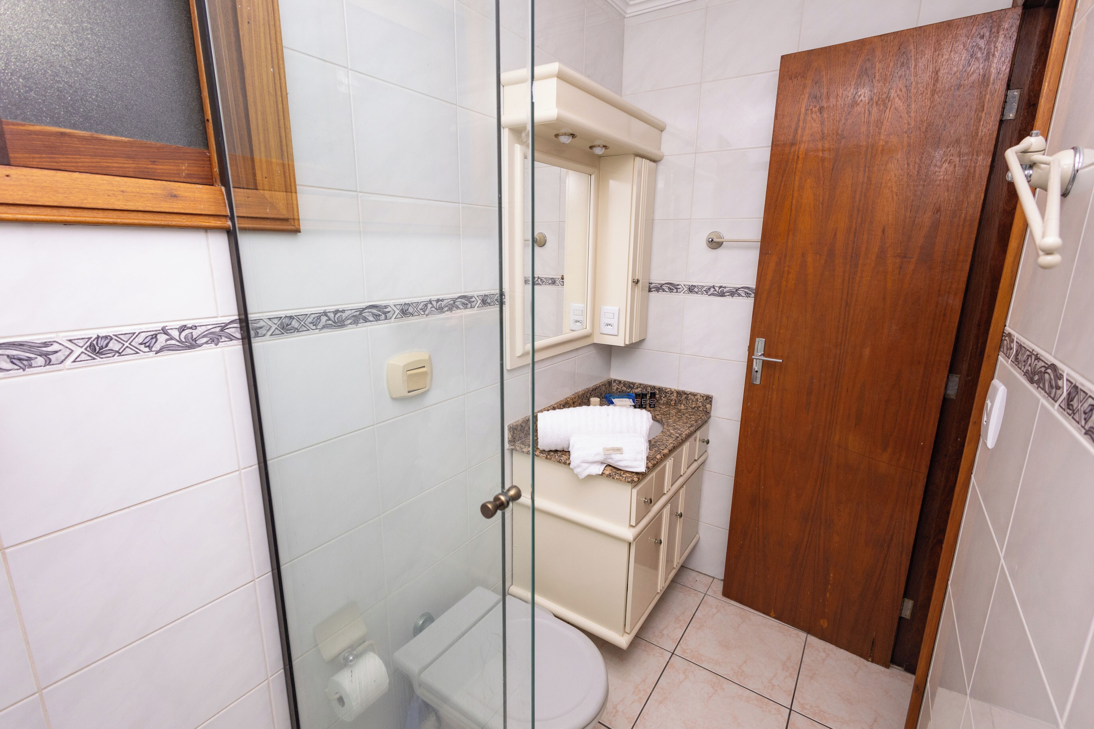Un bagno con box doccia in vetro, un water, un lavandino con un asciugamano e una porta in legno.