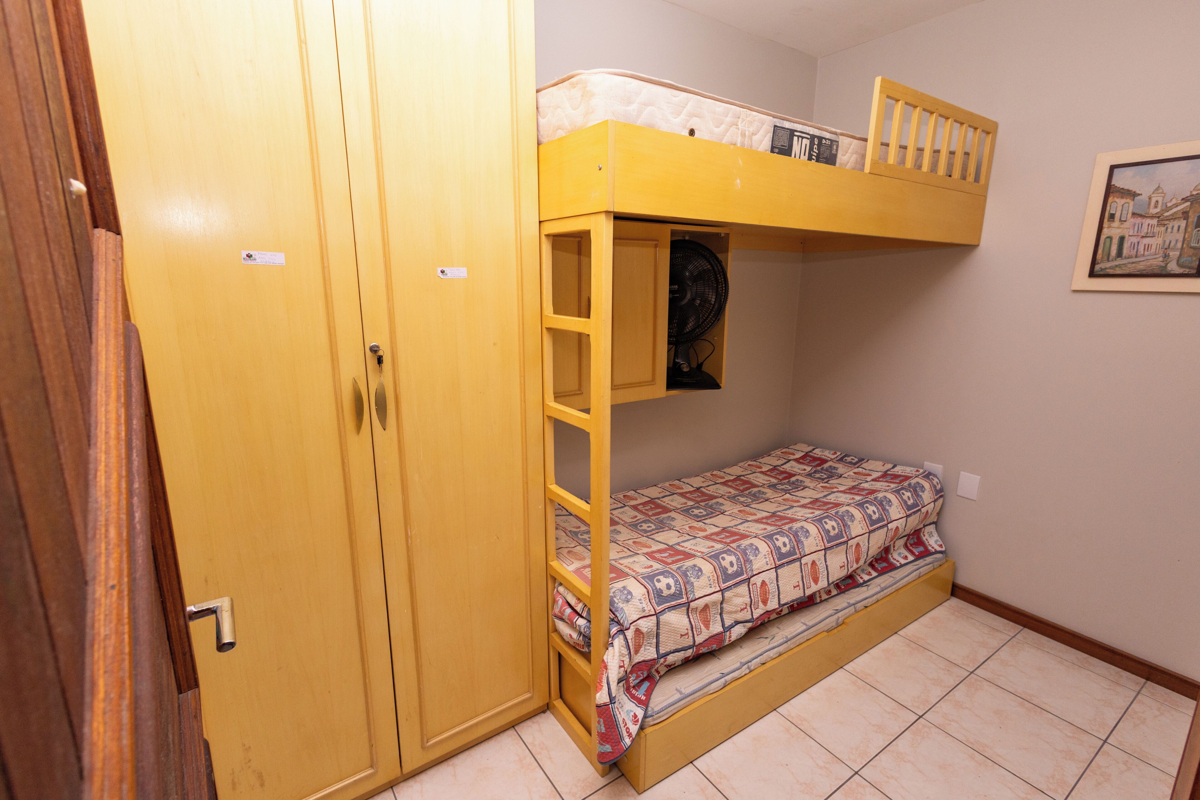 A room with a bunk bed, a wardrobe, and a framed picture on the wall.