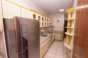 A compact kitchen with a stainless steel refrigerator, wooden cabinets, a sink, and a clock on the wall.