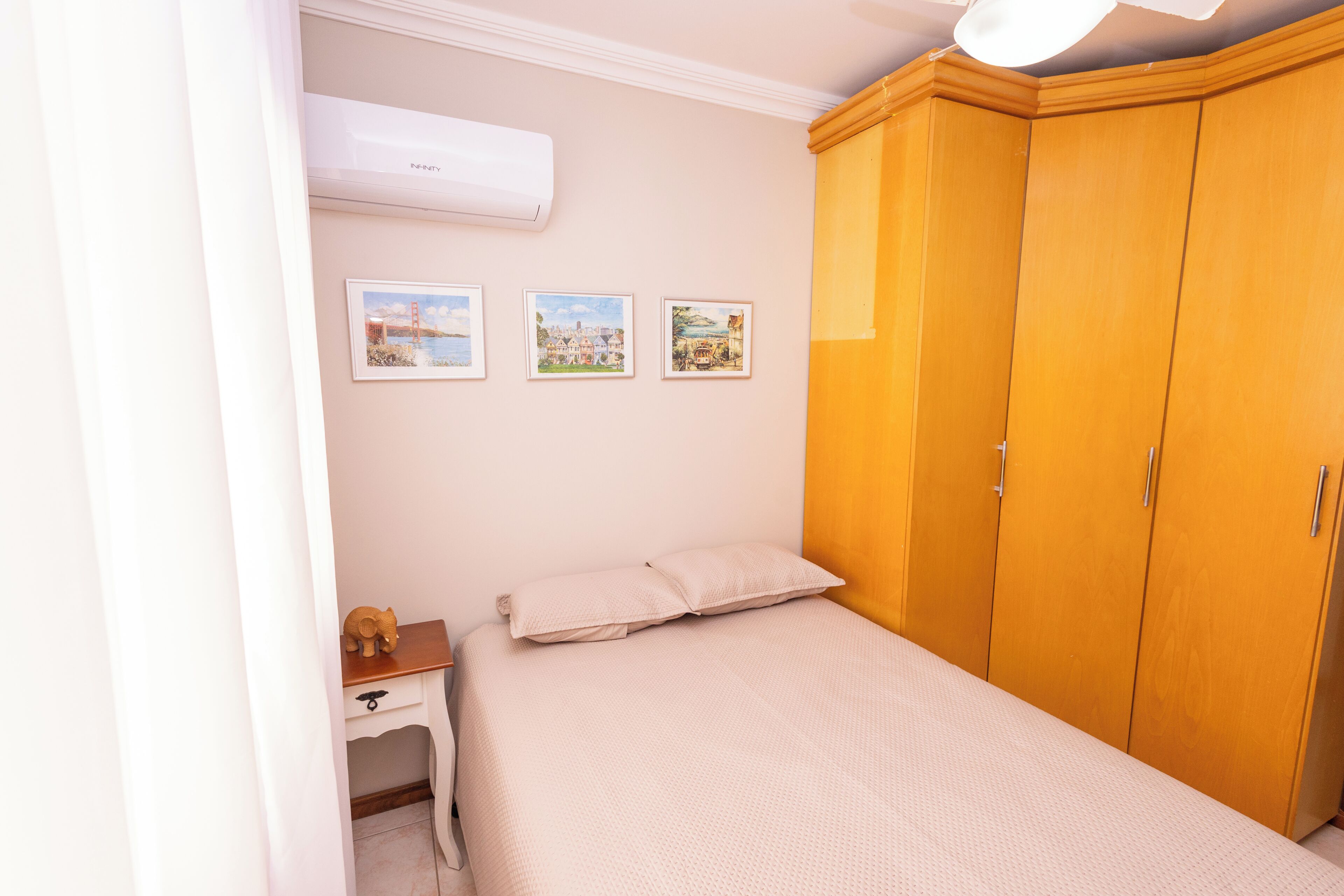 Un dormitorio con una cama, un armario, una mesita de noche y tres cuadros en la pared.
