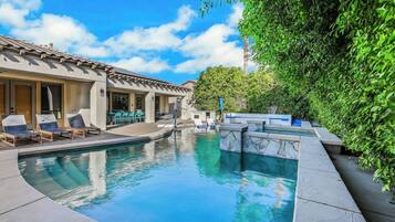A swimming pool with lounge chairs and a covered seating area, surrounded by greenery.