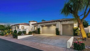 A two-story house with a garage, a driveway, and a well-maintained garden with shrubs and a palm tree.