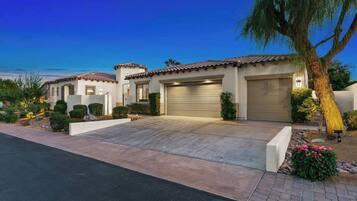 A two-story house with a garage, a driveway, and a well-maintained garden with shrubs and a palm tree.
