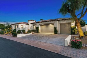 A two-story house with a garage, a driveway, and a well-maintained garden with shrubs and a palm tree.