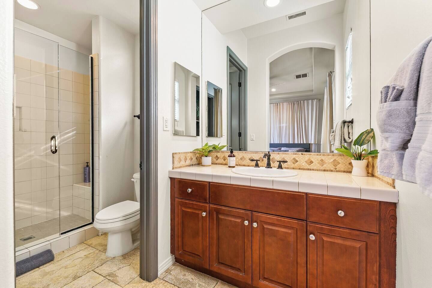 A modern bathroom with a glass shower enclosure, a white toilet, a wooden vanity with a sink, and a large mirror.