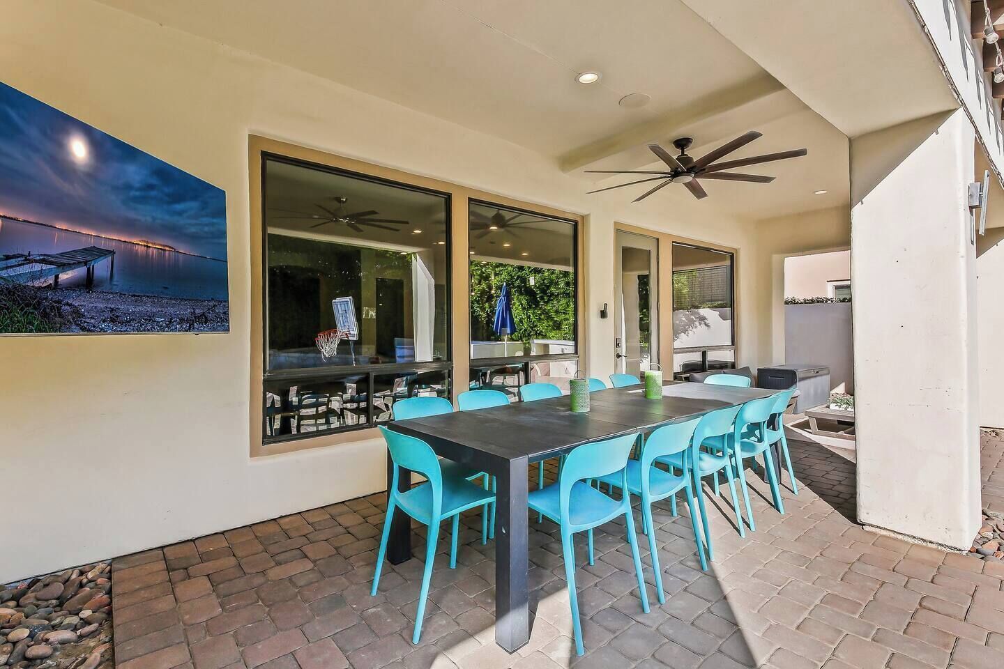 Un espace extérieur aménagé pour prendre les repas, avec une table et des chaises, de grandes fenêtres et un ventilateur de plafond.