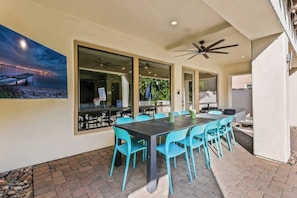 An outdoor dining area with a table and chairs, large windows, and a ceiling fan.