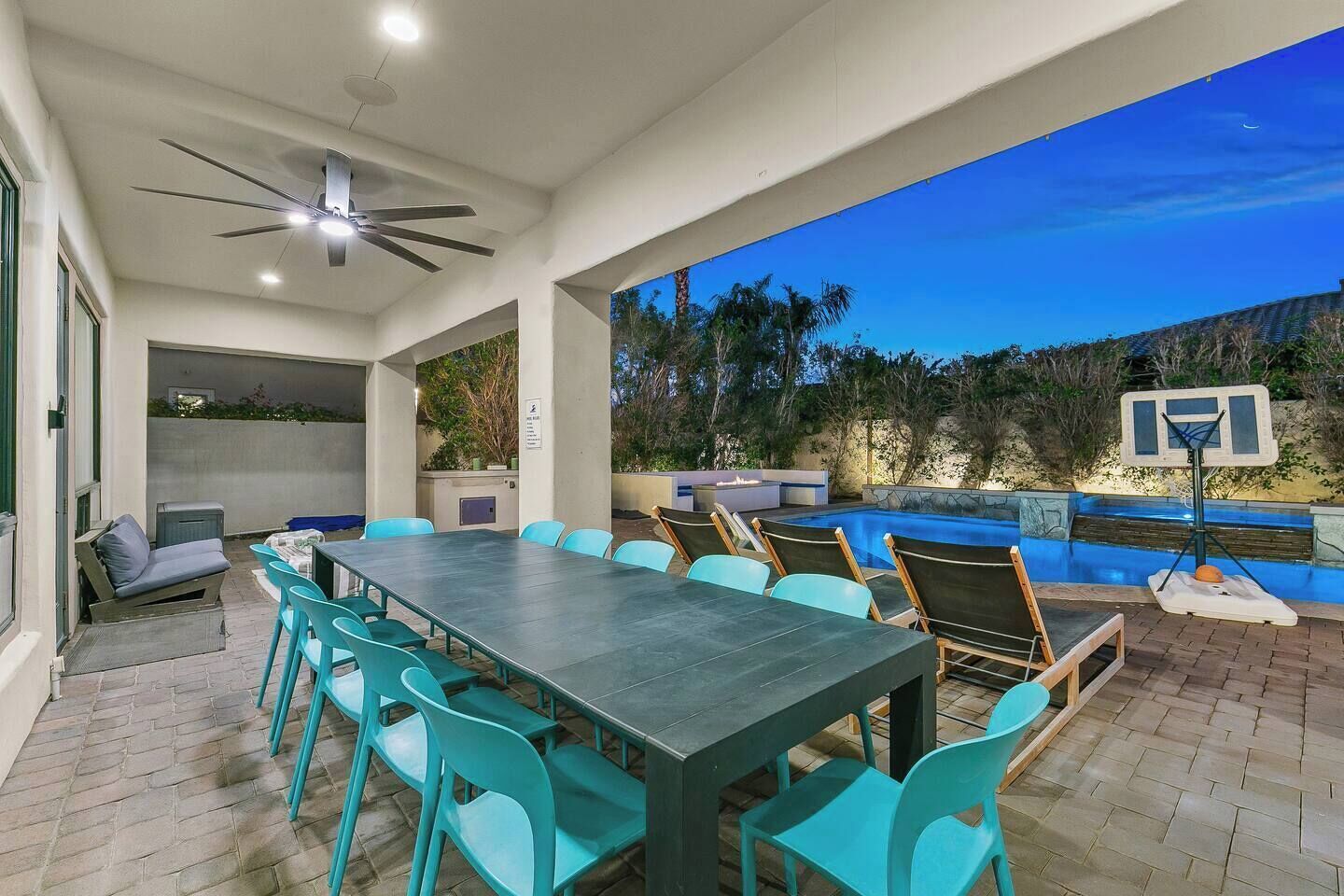 Um pátio externo com mesa e cadeiras para refeições, piscina e cesta de basquete.