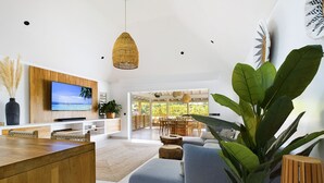 Uma sala de estar moderna com uma televisão grande, uma mesa de centro de madeira e uma planta exuberante.