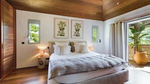 Quarto moderno com cama grande, soalho de madeira e vista para o verde pelas janelas.