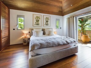 Ein modernes Schlafzimmer mit einem großen Bett, Holzboden und Blick auf Grün hinter den Fenstern.