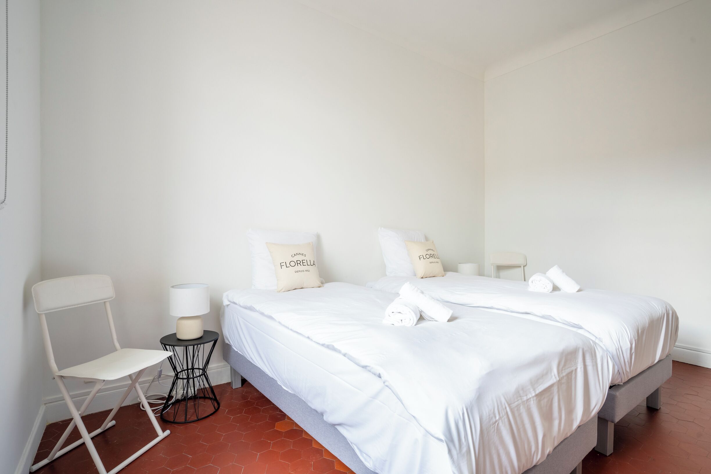 A hotel room with two beds, a chair, a small table, and a lamp.