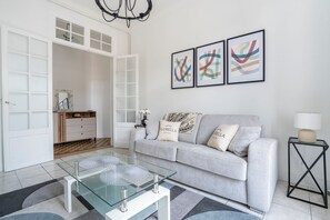 A modern living room with a glass coffee table, grey sofa, and abstract wall art. - Les Tomettes d'Antan avec balcon en plein Cannes (Cannes)